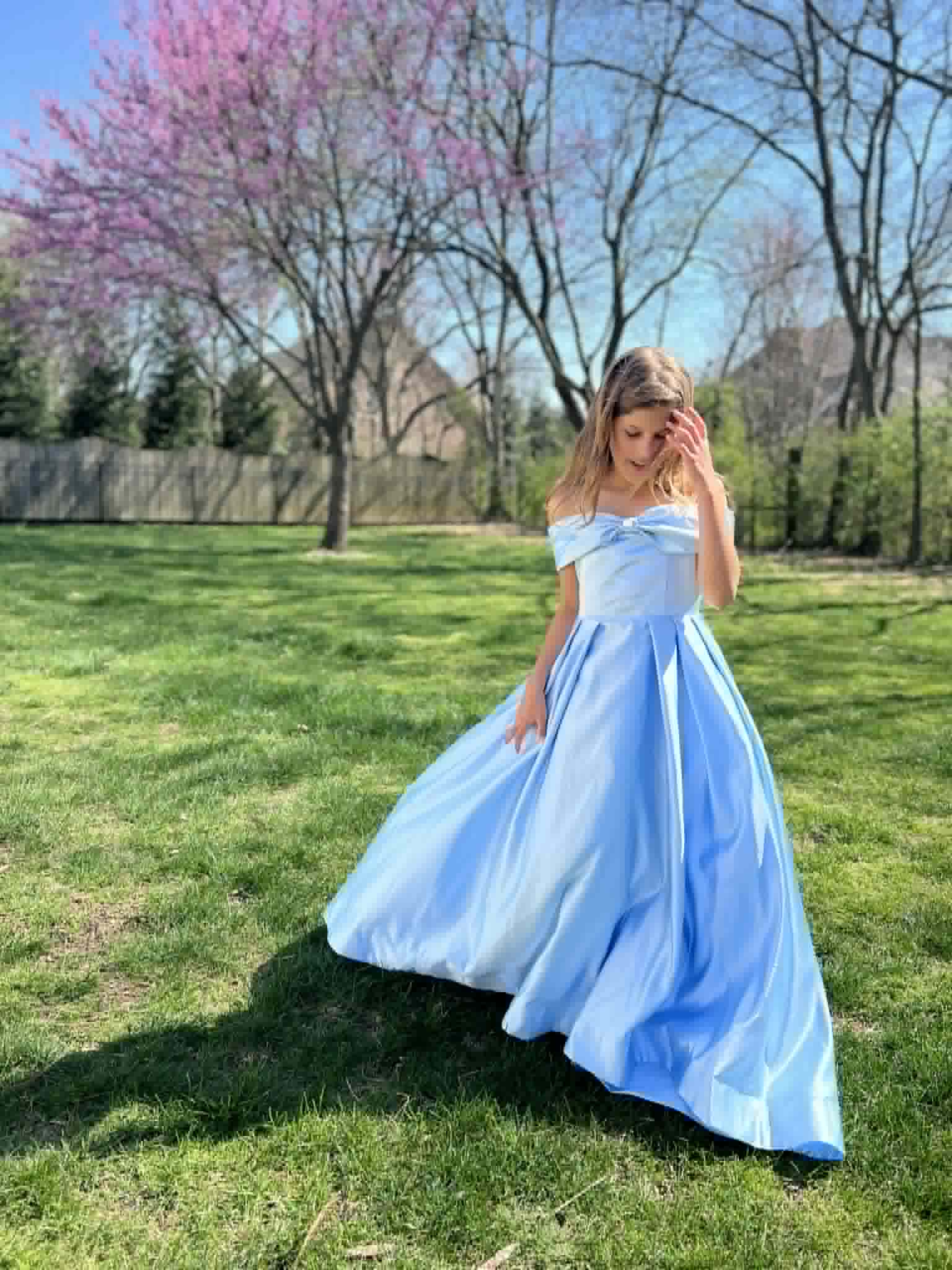 A little girl modeling a big, blue princess dress in her backyard.
