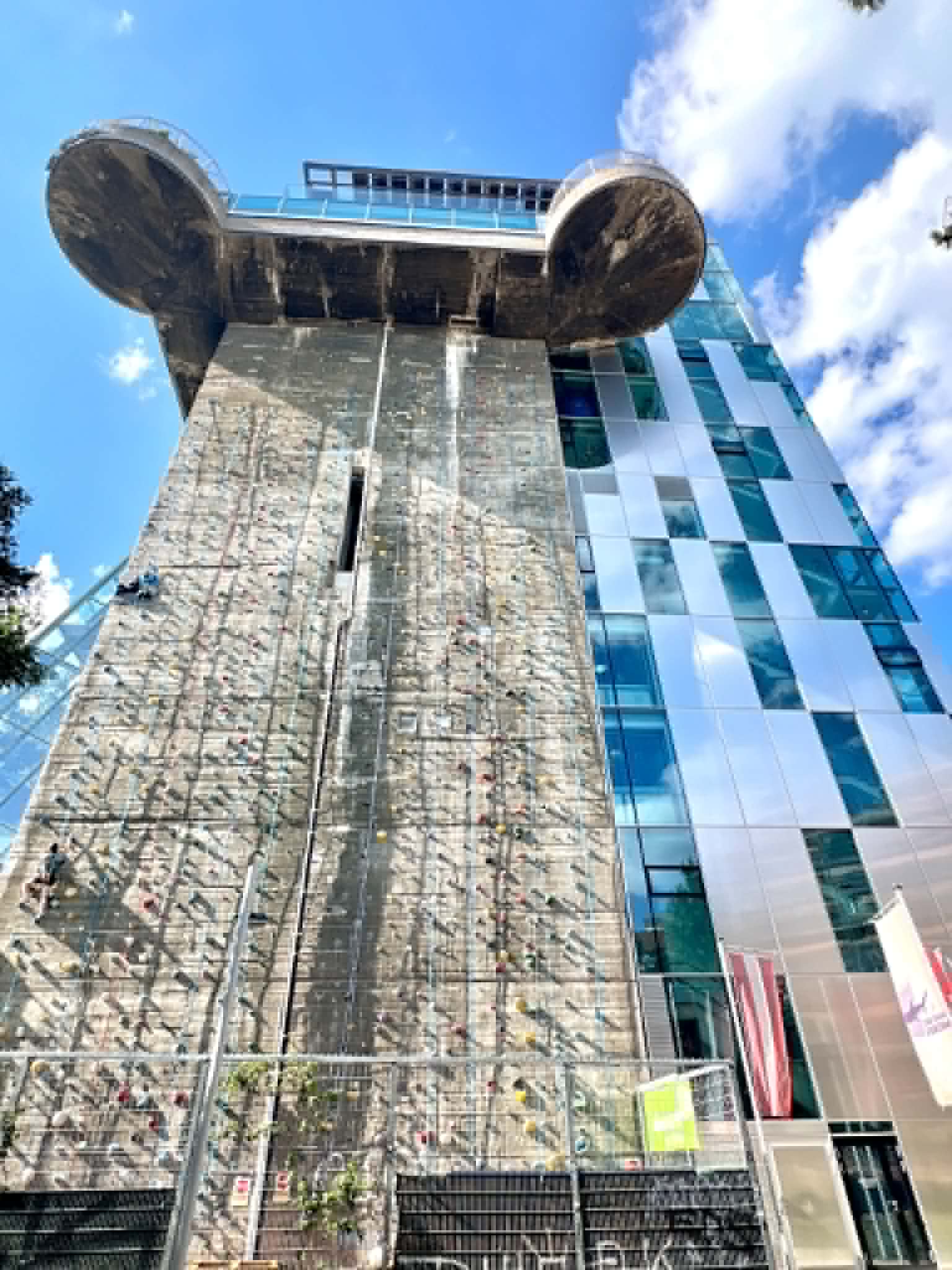 Building with rock climbing wall and glass building next to it.