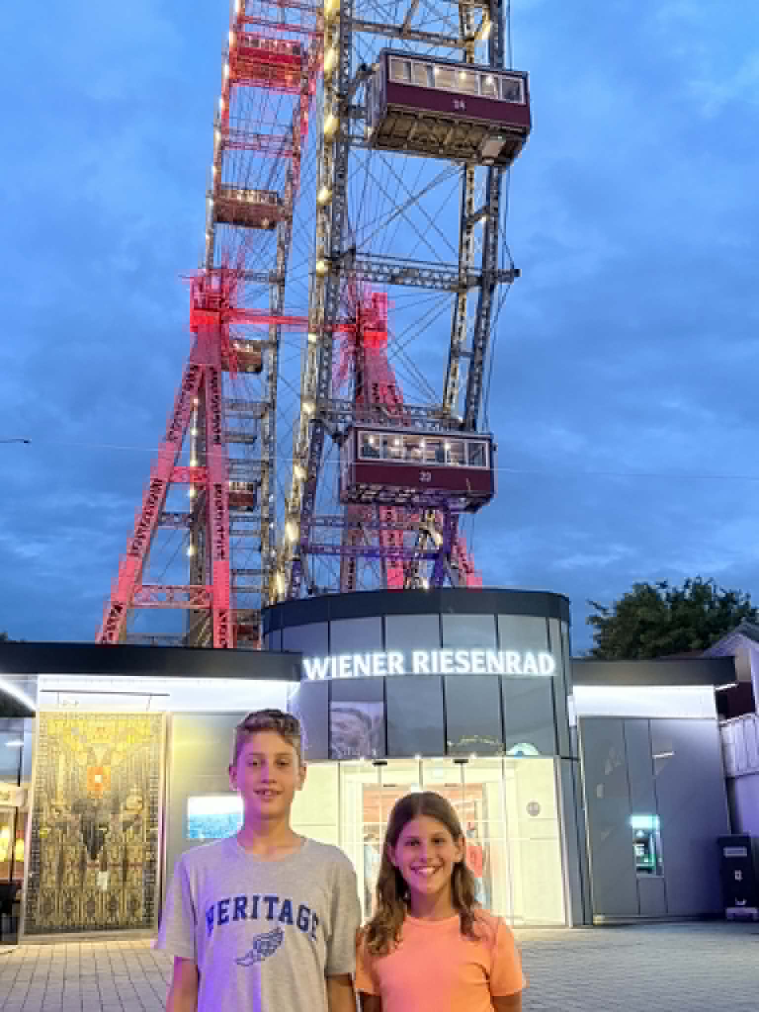 Girl and boy in front, oldest Ferris wheel in the world in the back.