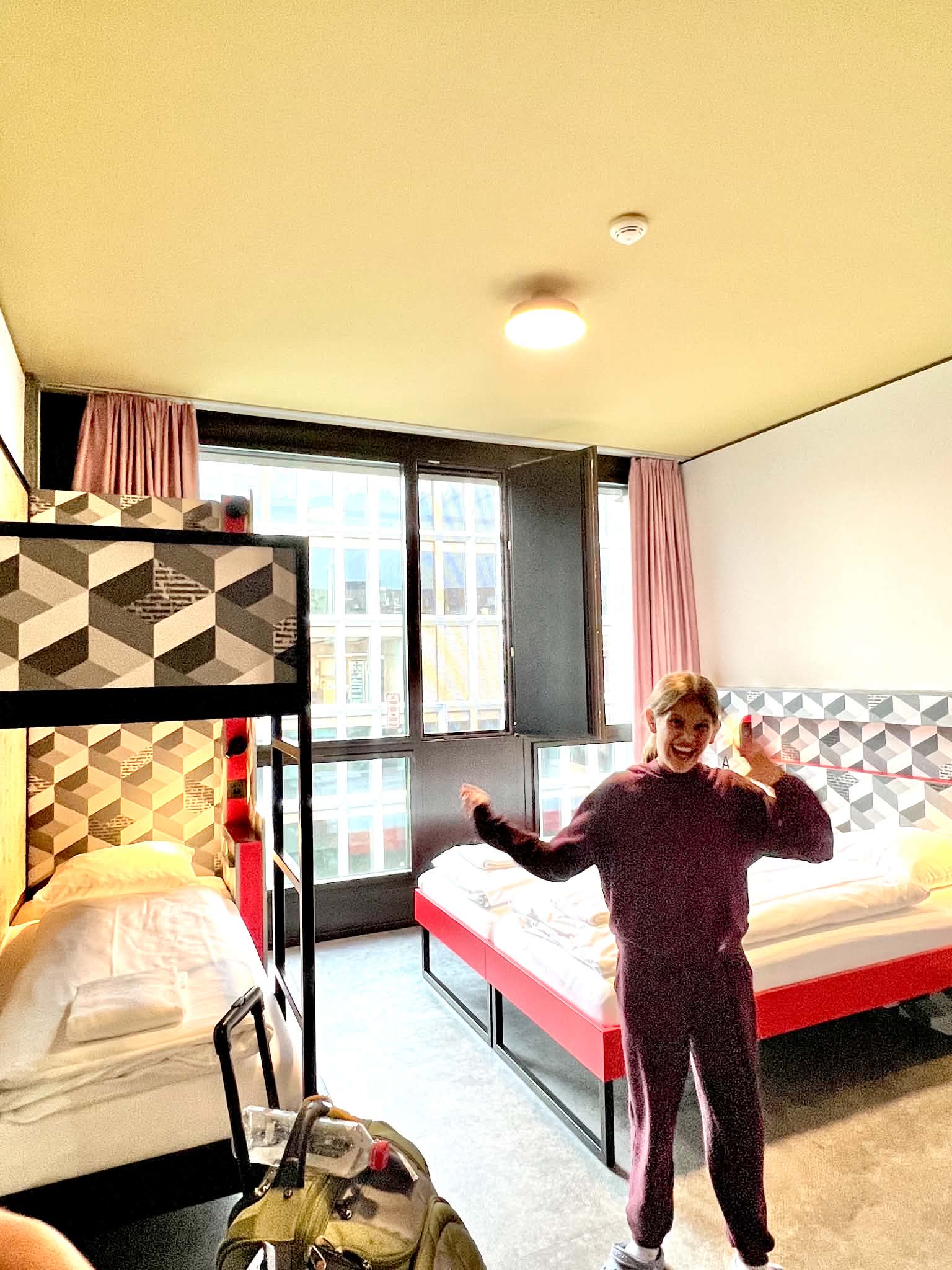 A little girl with her hands up inside her hotel room at Meininger hotel. There are bunk beds and a queen size bed.
