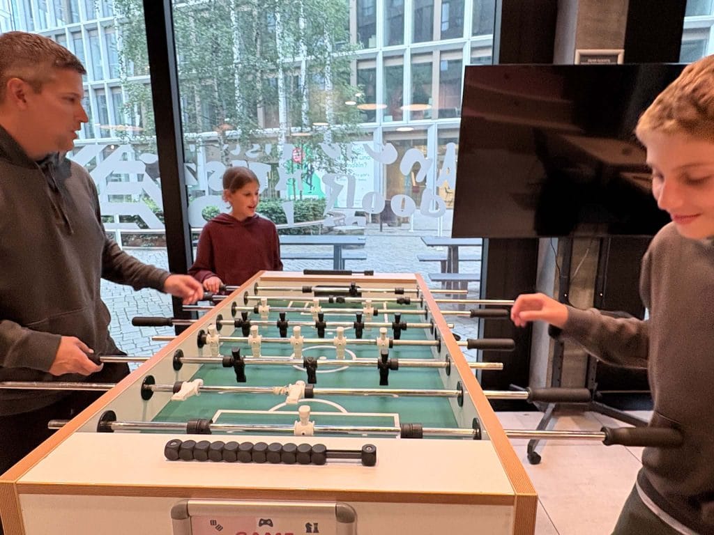 A dad and two kids playing Foosball at the Meininger hotel in Zurich. 