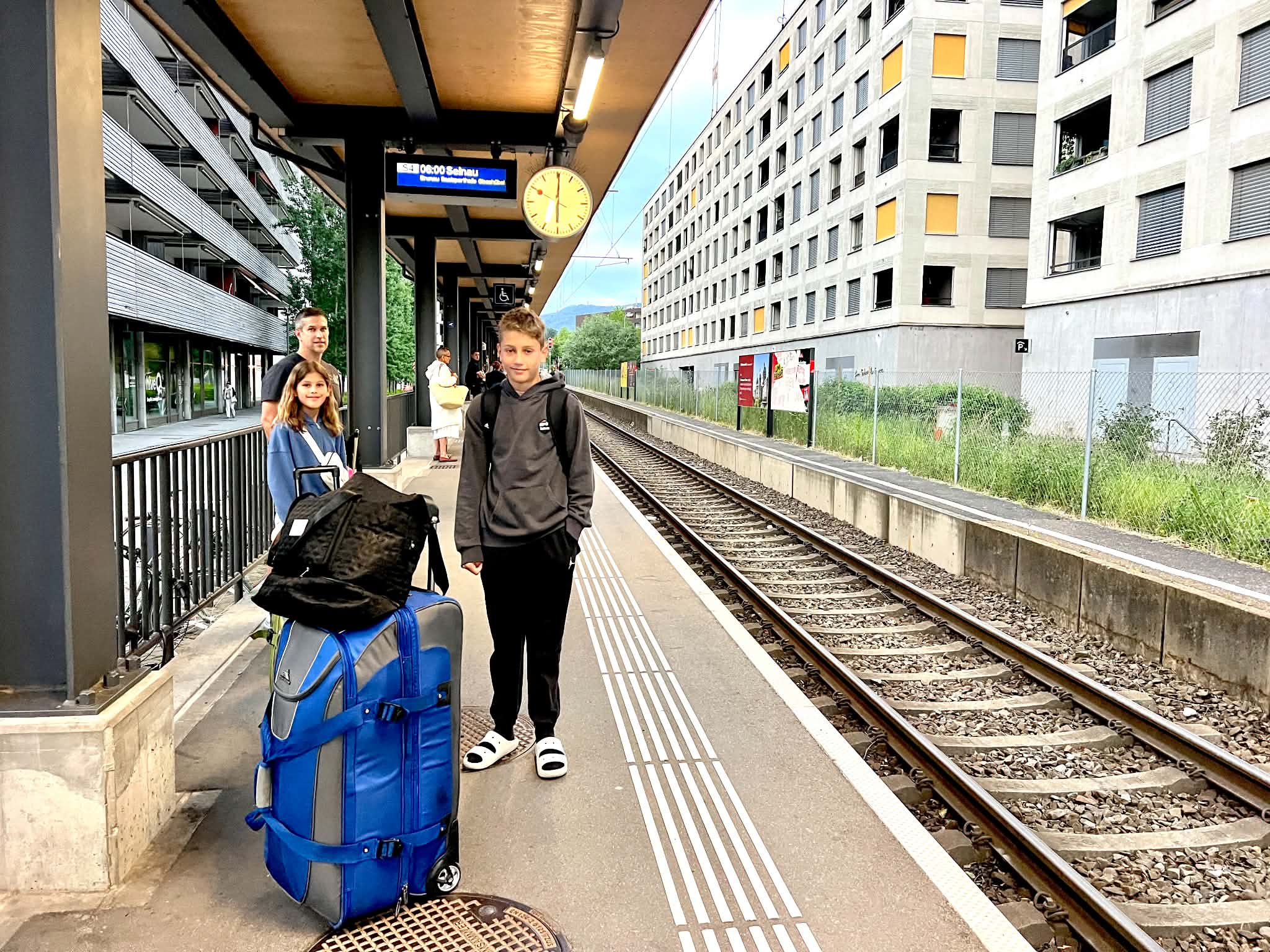 A dad and two kids on the Zurich train platform with their suitcases. 