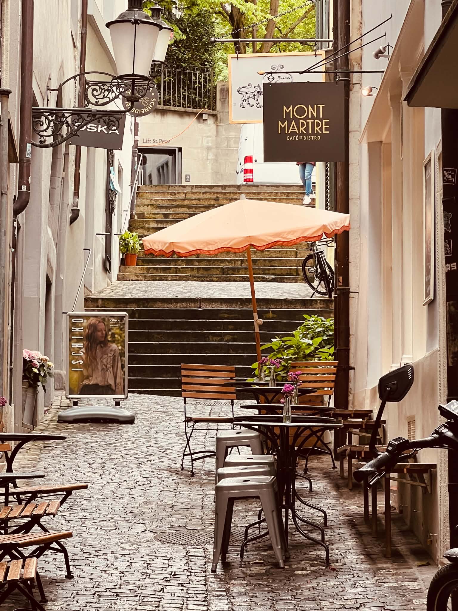 A beautiful little alleyway in Old Town, Zurich, Switzerland where there is a peach colored umbrella at the Montmartre Cafe.