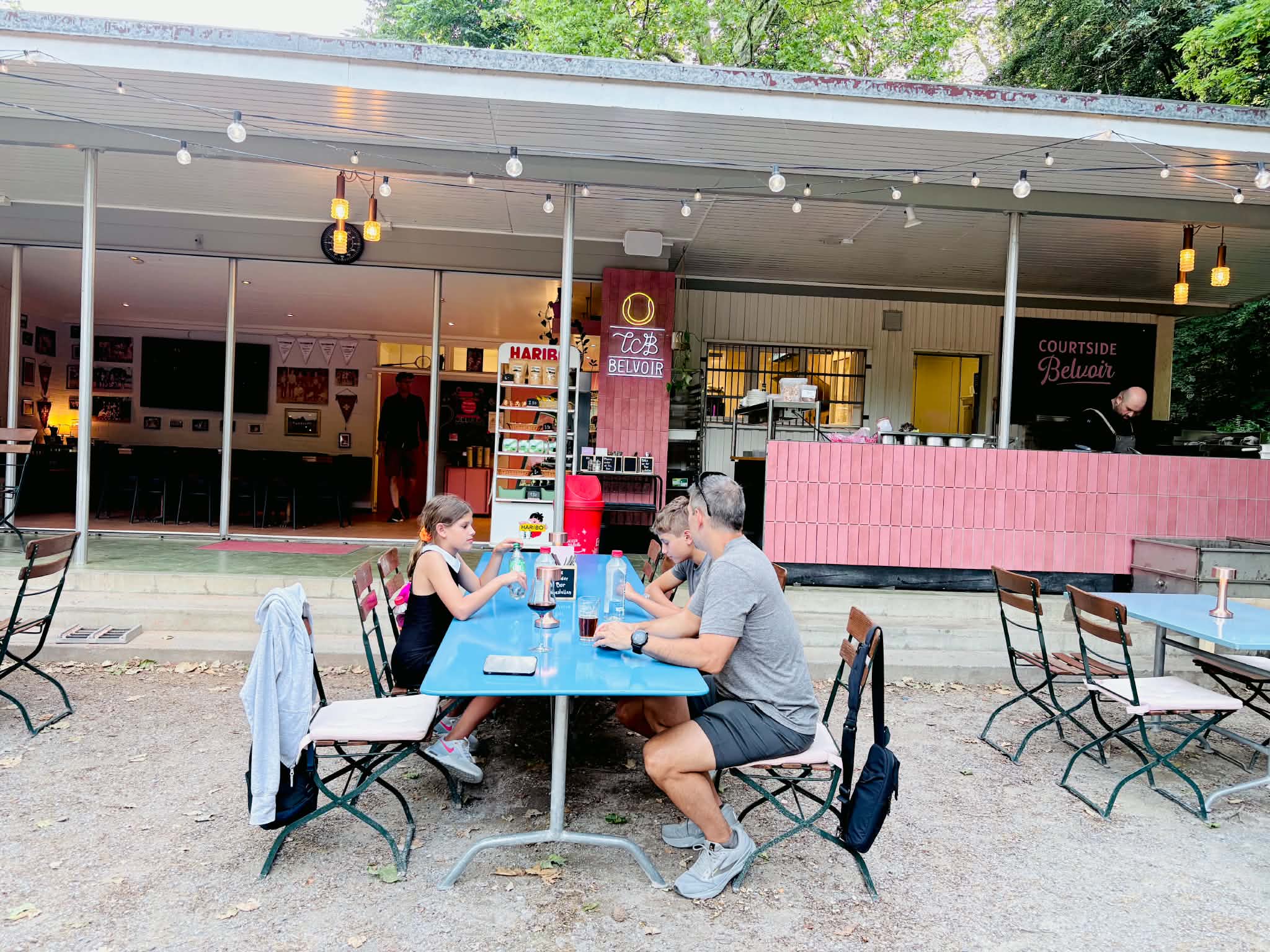 A dad and two kids sitting at their outdoor table at Courtside Belvoir in Zurich, Switzerland.