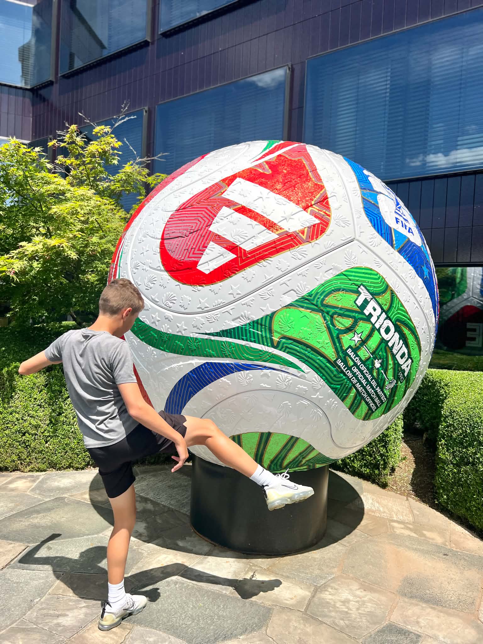 A teenage boy pretending to kick the massive soccer ball that is outside the FIFA Museum in Zurich, Switzerland.