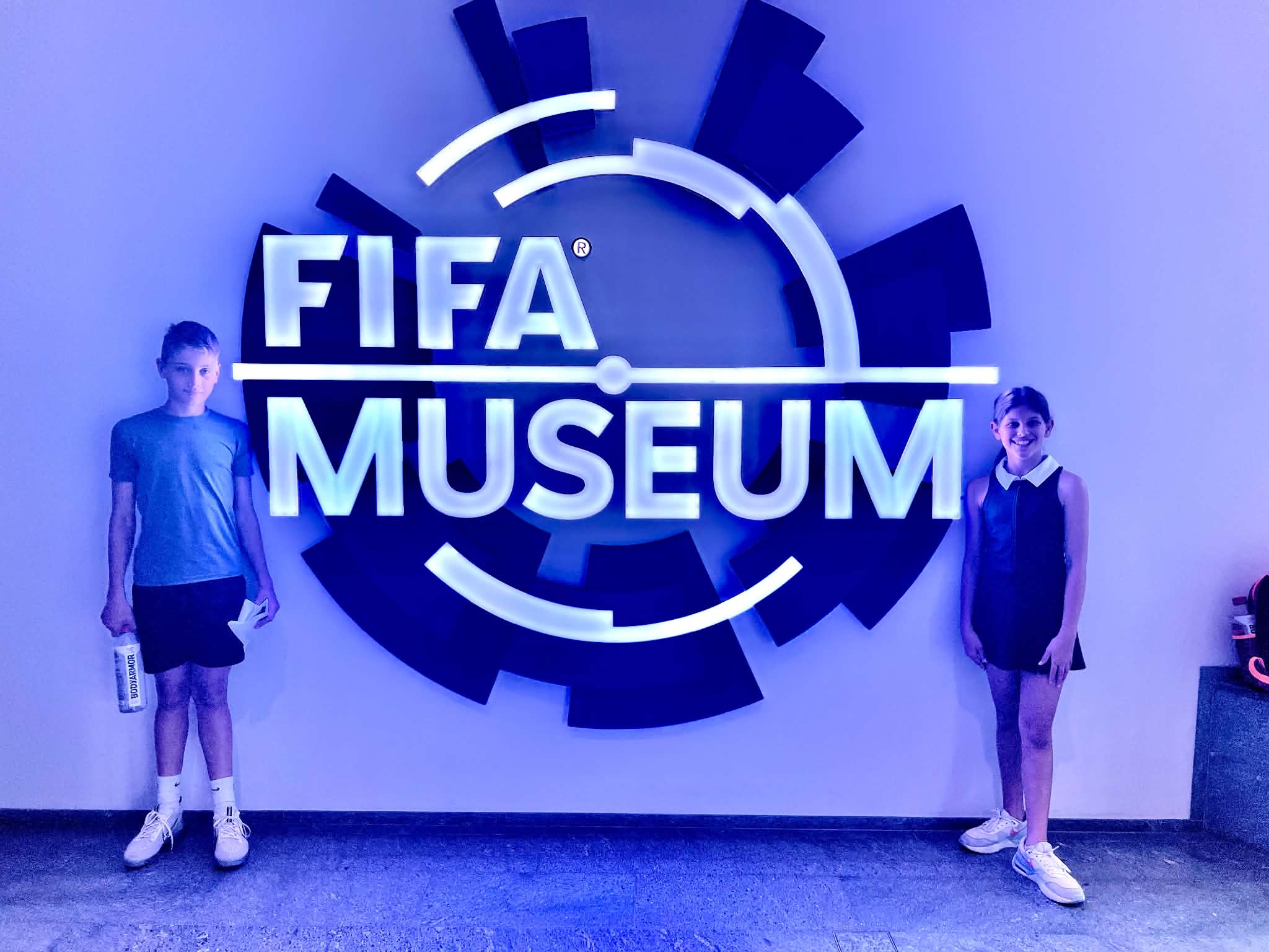 Two kids standing next to the FIFA Museum sign in Zurich, Switzerland.