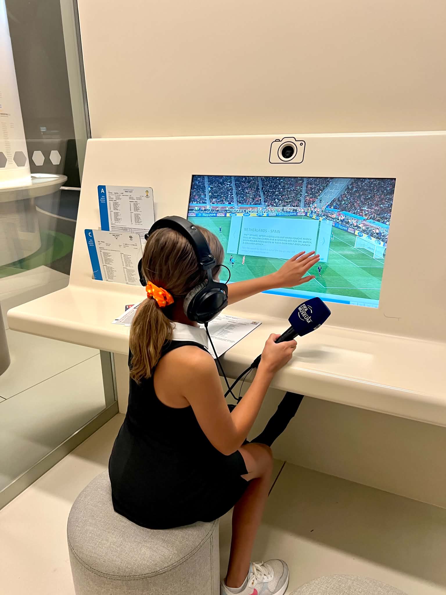 A kid acting as the sports broadcaster during a soccer game at the FIFA Museum.