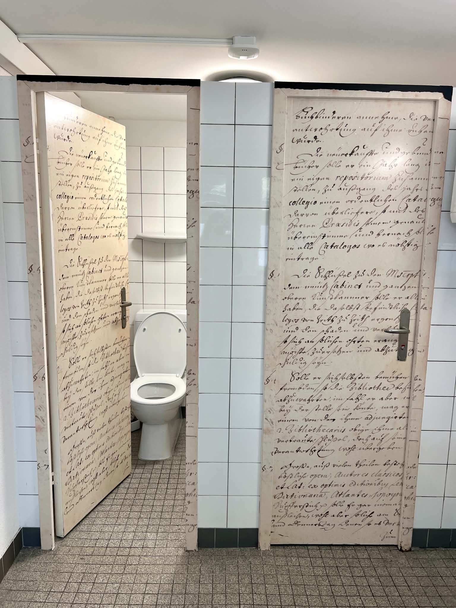 Two bathroom doors in the Zurich Library that has old, cursive words written across them.