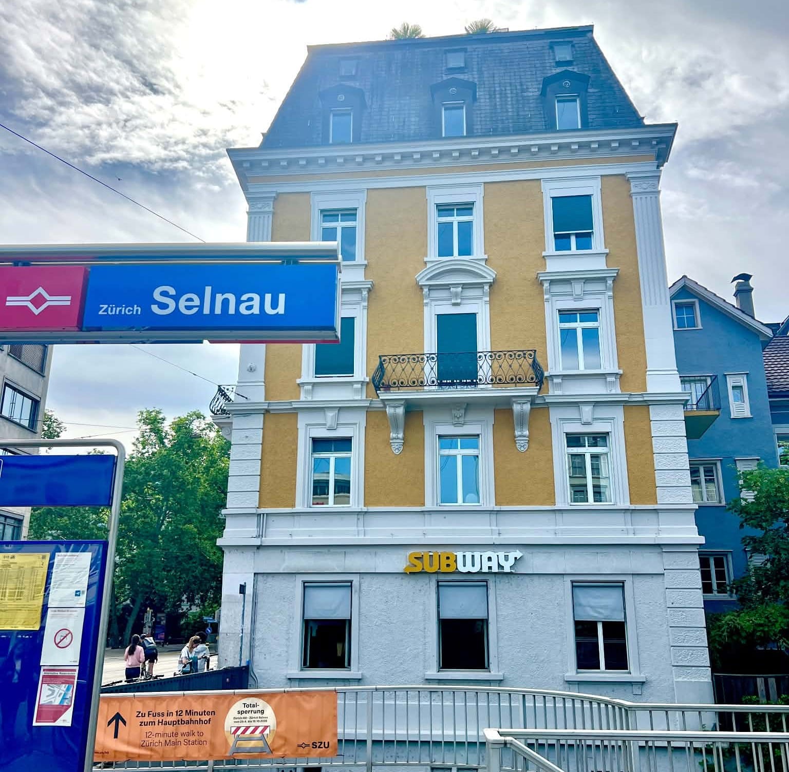 A 5 story yellow and white building that houses a Subway restaurant on the first floor in Zurich.