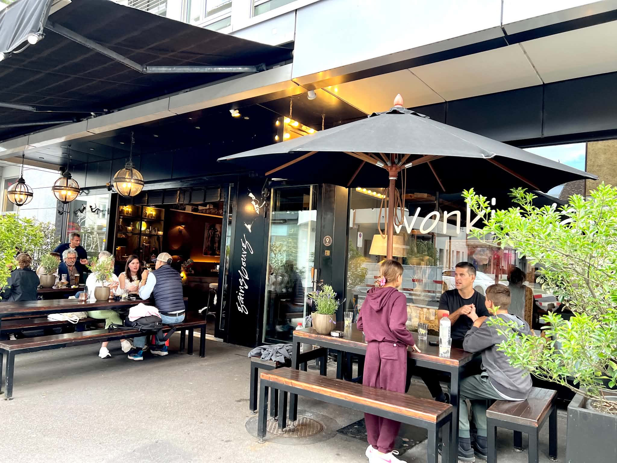 Outdoor picnic tables with people all around them at Gainsbourg Mexican Restaurant in Zurich. A dad is eating with his two kids.