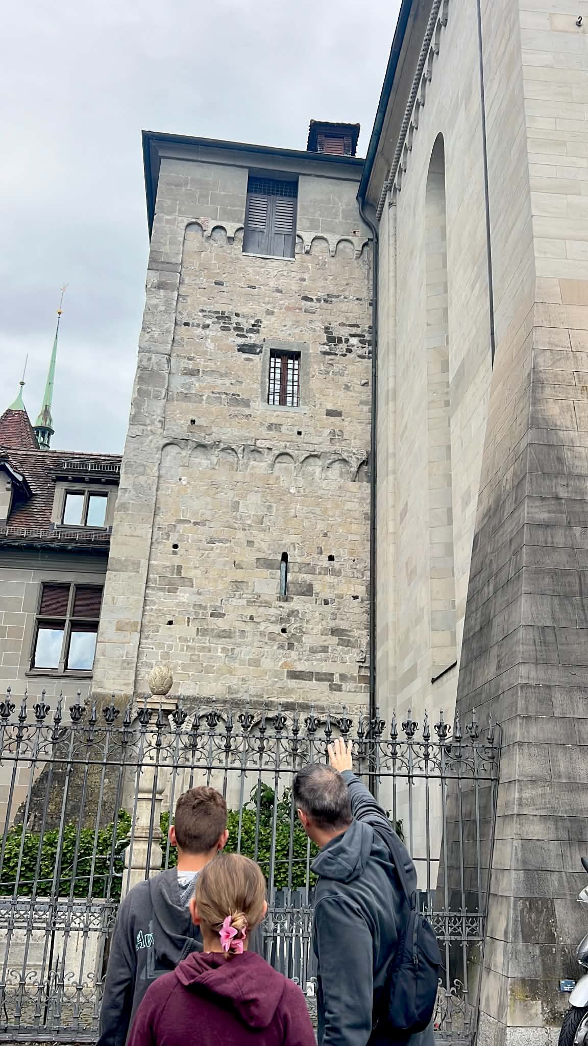 A dad showing his kids a really old building in Zurich, Switzerland. He is pointing to the stone.