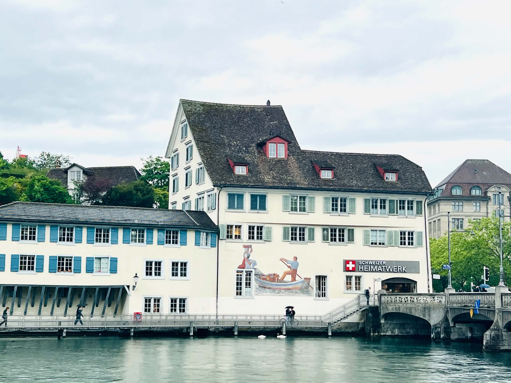 A white building with blue shutters on Lake Zurich. On the building is a painting of a boat.
