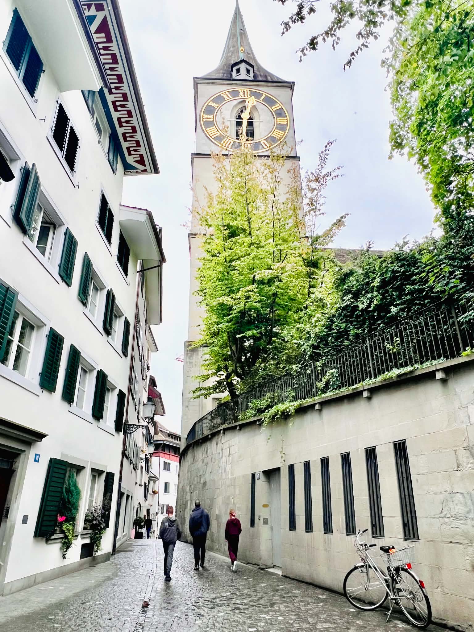 A dad and two kids walking in Old Town, Zurich, Switzerland with a huge clock tower in front of them.