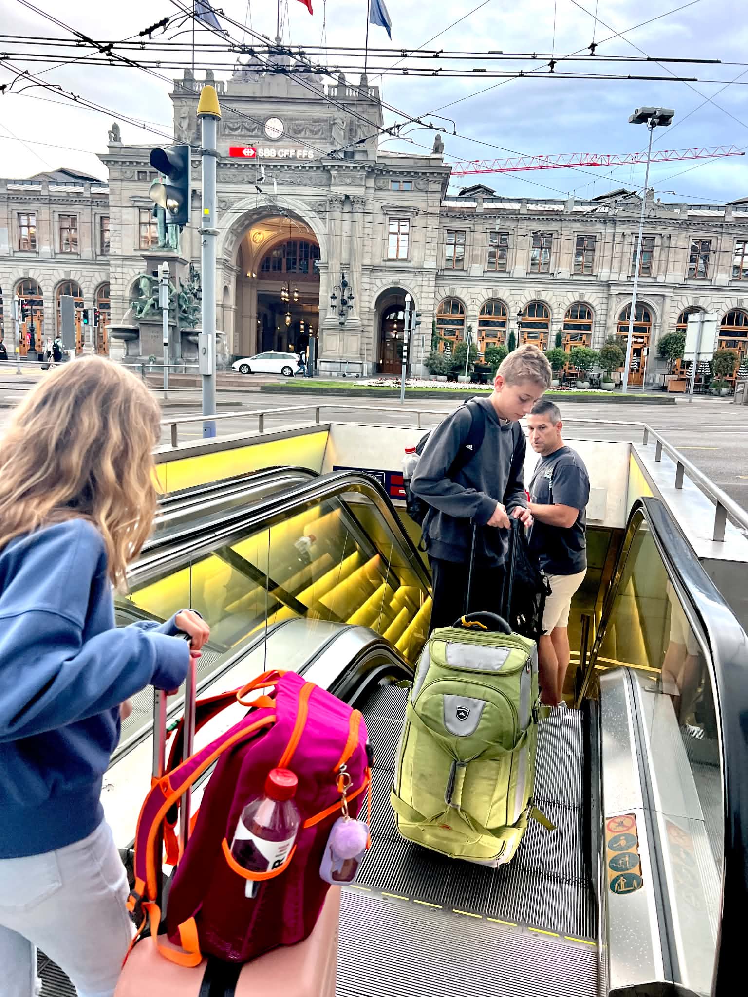 A dad in Zurich with kids navigating their suitcases down to the train station.