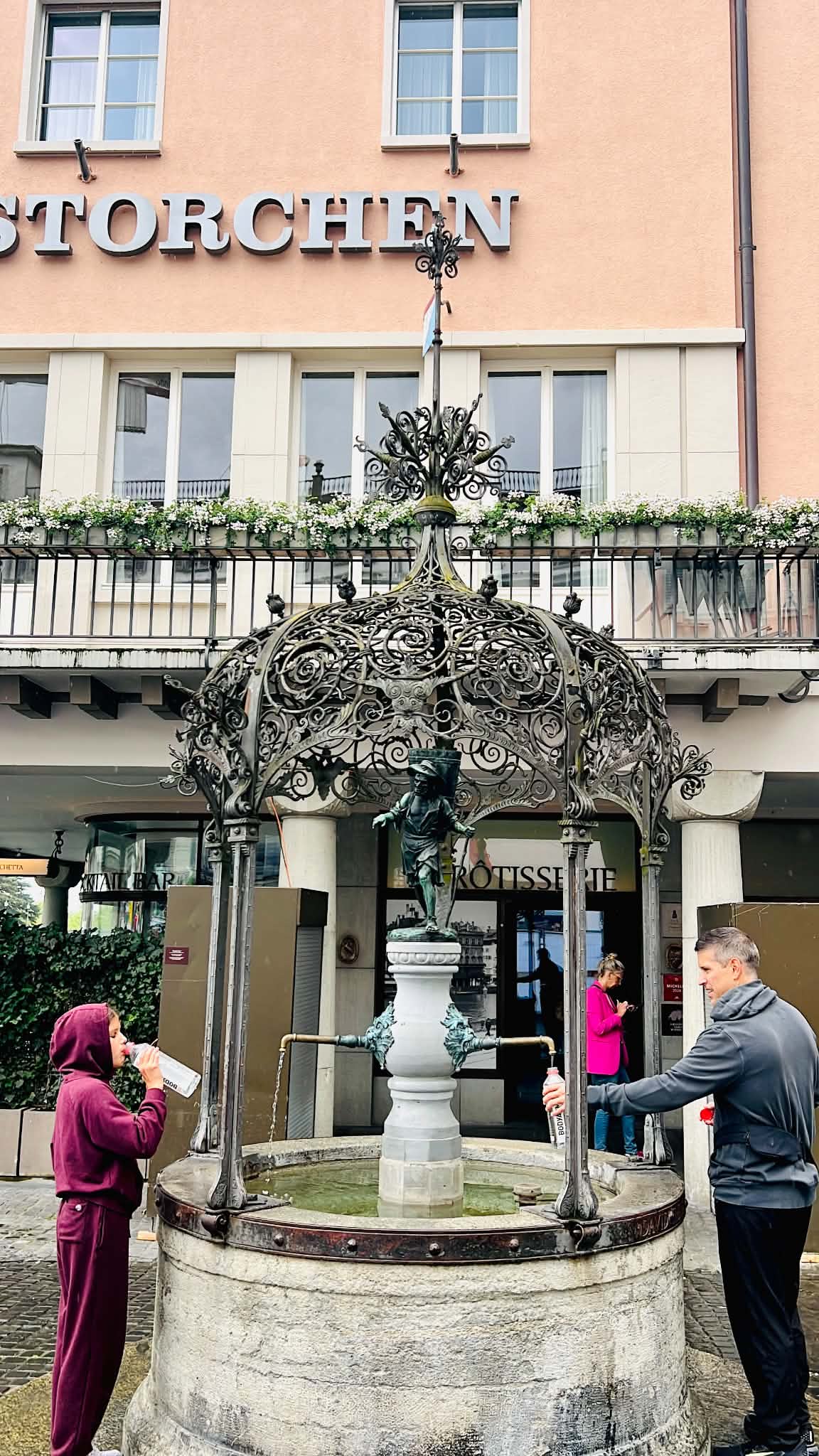 A dad and daughter filling up their water bottles at a free, beautiful water fountain in Zurich.