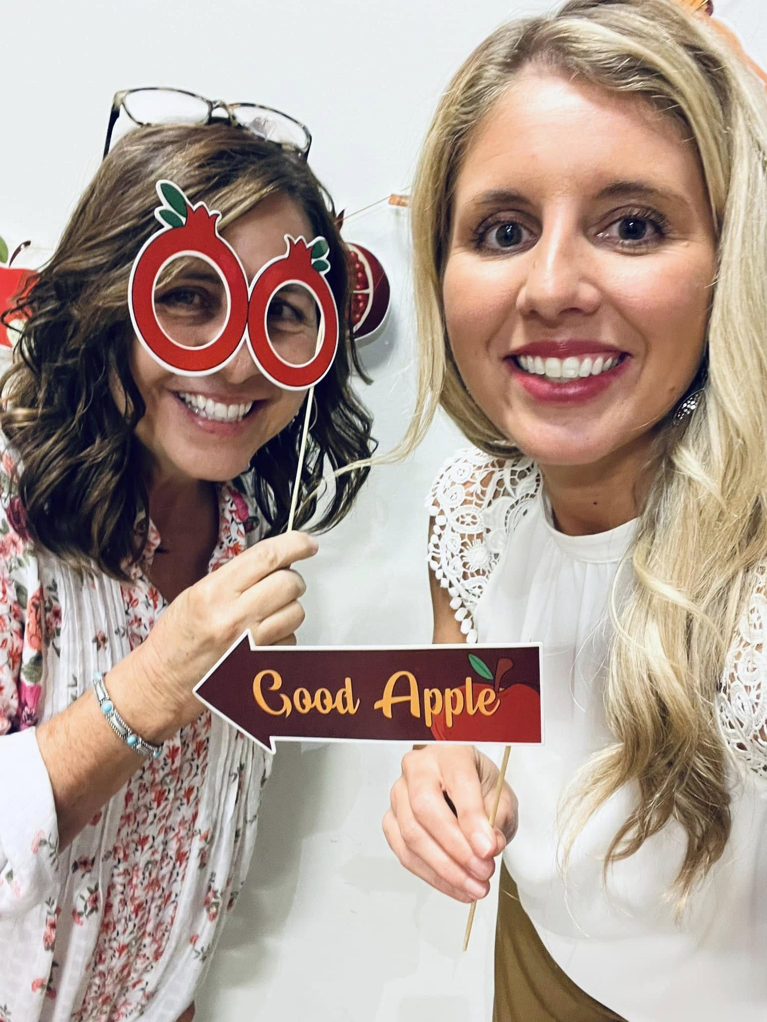 Two more girls playing with the photo props. One has the pomegranate glasses and the other has a sign saying, "Good apple".