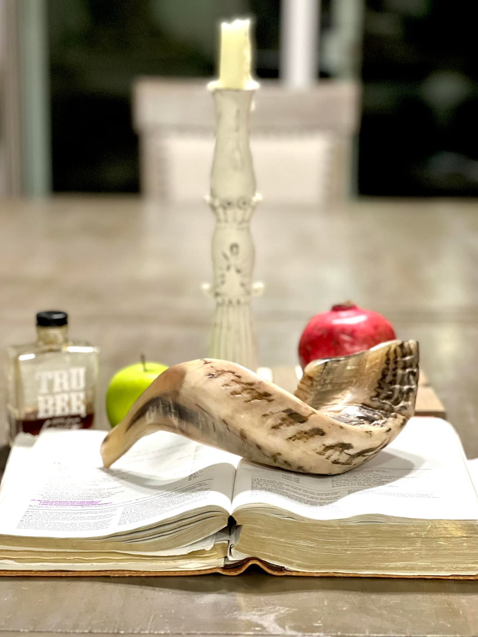 Feast of Trumpets is all about Jesus - a Bible with a shofar sitting on top of it. A candle, honey and a pomegranate are behind it.