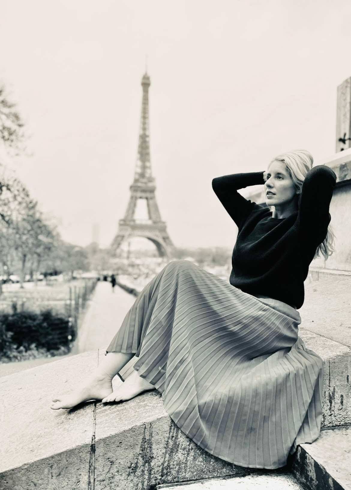 Black and white photo of girl sitting on the steps with the Eiffel Tower behind her in Paris, France.